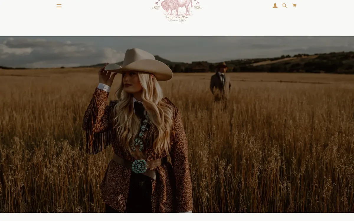 Hero photograph of a woman in a leopard-print fringe jacket and turquoise squash-blossom necklace touching her cowboy hat in a golden field, with a man in the background, and no text or buttons over the image